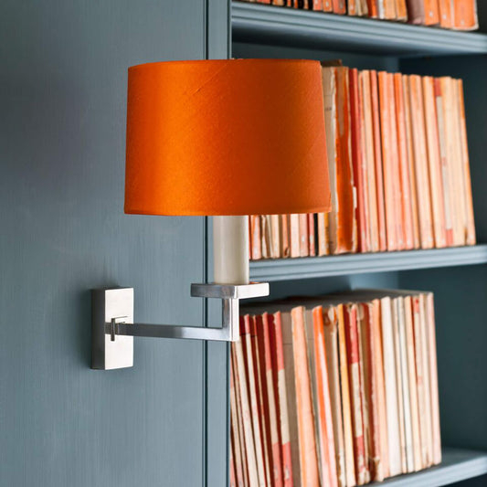 Fixed library wall light in chrome with an orange silk shade mounted on a grey bookcase